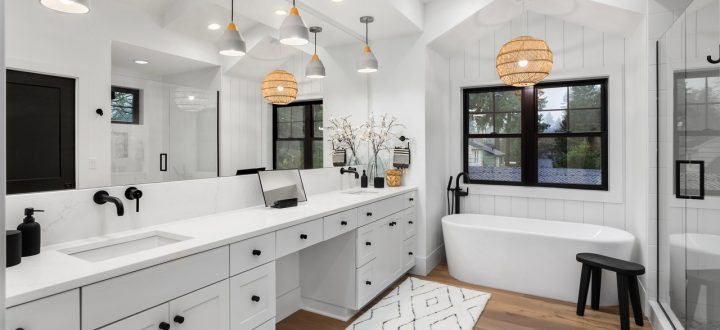 Modern bathroom featuring a freestanding tub, white vanity with dual sinks, and pendant lighting, accentuated by wooden floor and chic decor.