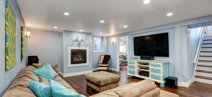 A warmly decorated family room in a basement with a plush sectional sofa, wooden flooring, and a built-in fireplace, complemented by soft lighting and contemporary decor.