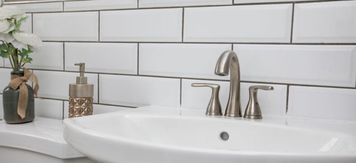 A minimalist bathroom featuring a clean white sink with modern faucet, set against classic white subway tiles and simple decor elements.